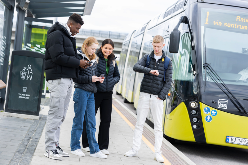 Fire elever på bussholdeplassen med buss i bakgrunnen
