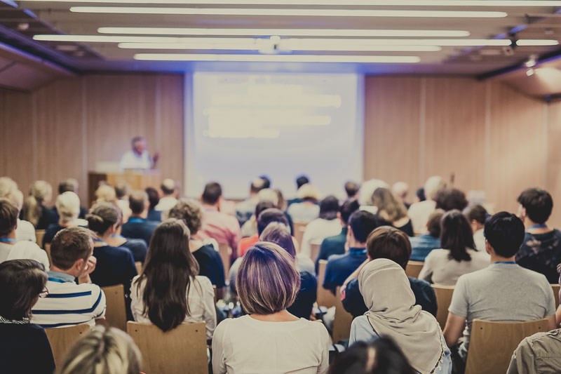 Illustrasjonsbilde fra Shutterstock som viser sal med personer i alle aldre som hører på PowerPoint-foredrag