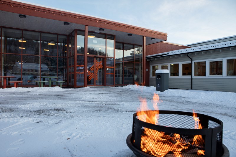 Bilde av skolens inngangsparti på vintertid, med brennende bålpanne i forgrunnen.