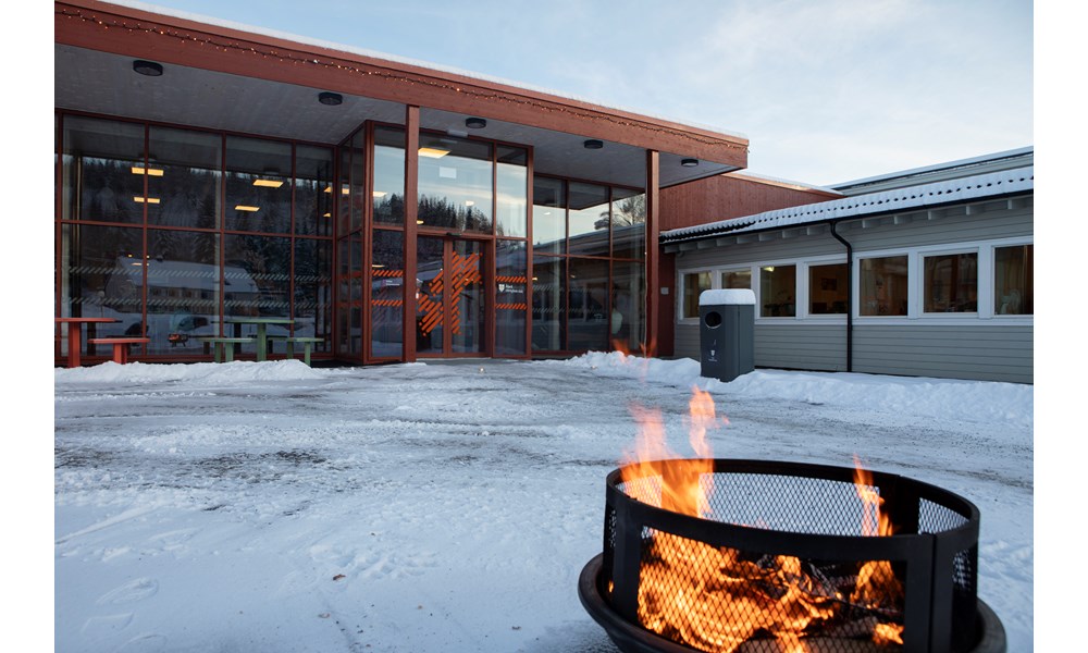 Bilde av skolens inngangsparti på vinteren med tent bålpanne i forgrunnen.