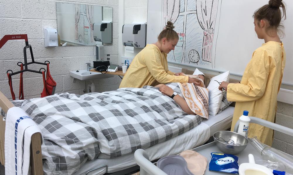 HA 2.jpg Ein elev ligg i senga og er "pasient", og ein annan elev trener på arbeidsoppgåver relevante for ein helsearbeidar.