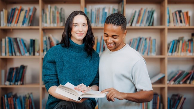 To personer smiler og blar i en bok i et bibliotek