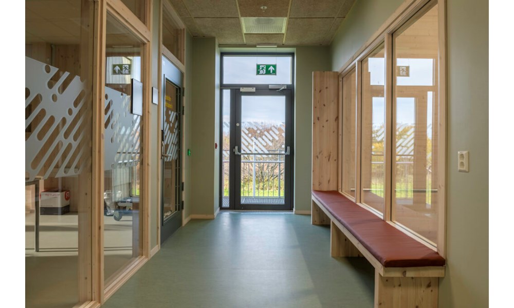 Bildet viser en korridor eller et venteareal preget av lyse trematerialer og store glassflater.