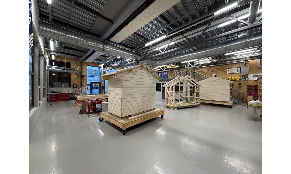 Dette bildet viser interiøret i en stor, moderne industrihall og er et verksted for byggfag eller tømrerarbeid.