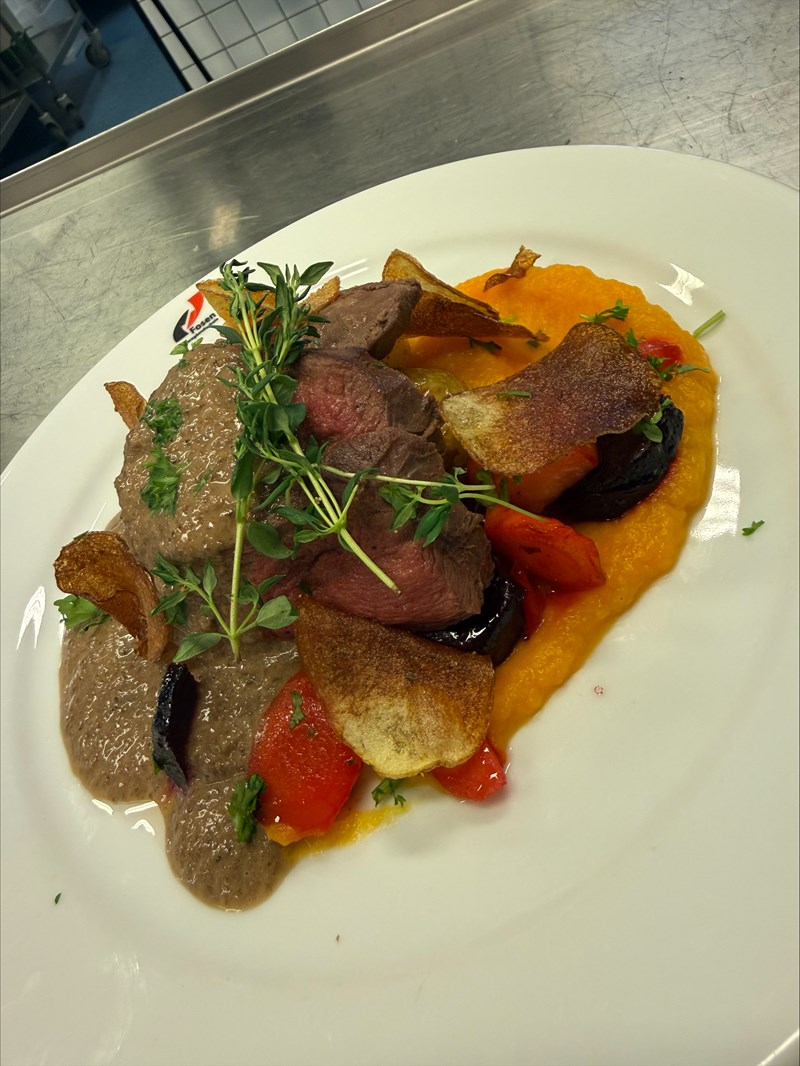 Dette bildet viser et nærbilde av en profesjonelt anrettet hovedrett på en hvit tallerken.