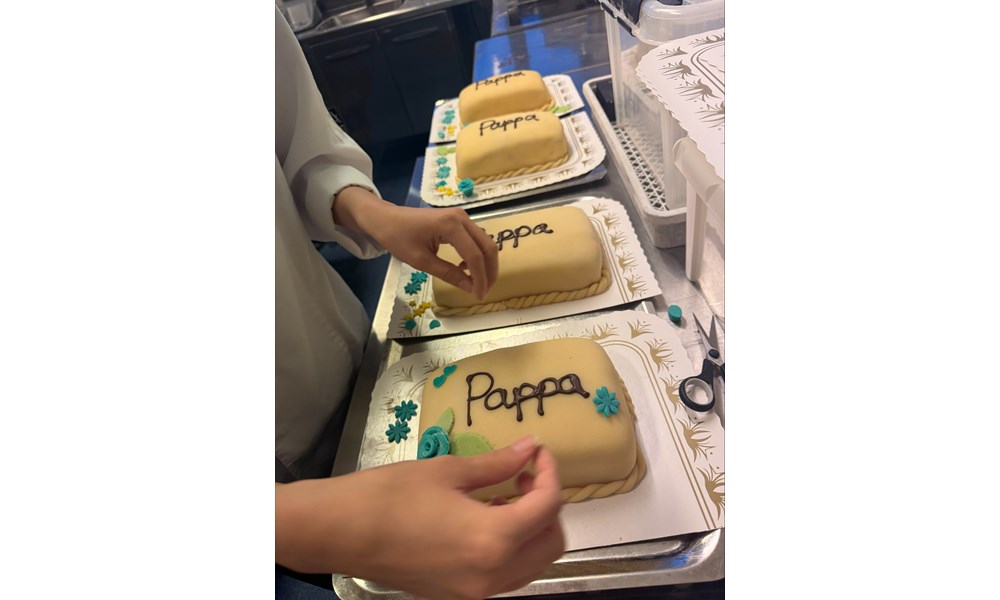 Dette bildet viser en person i hvit kokkejakke som legger siste hånd på verket på flere marsipankaker.