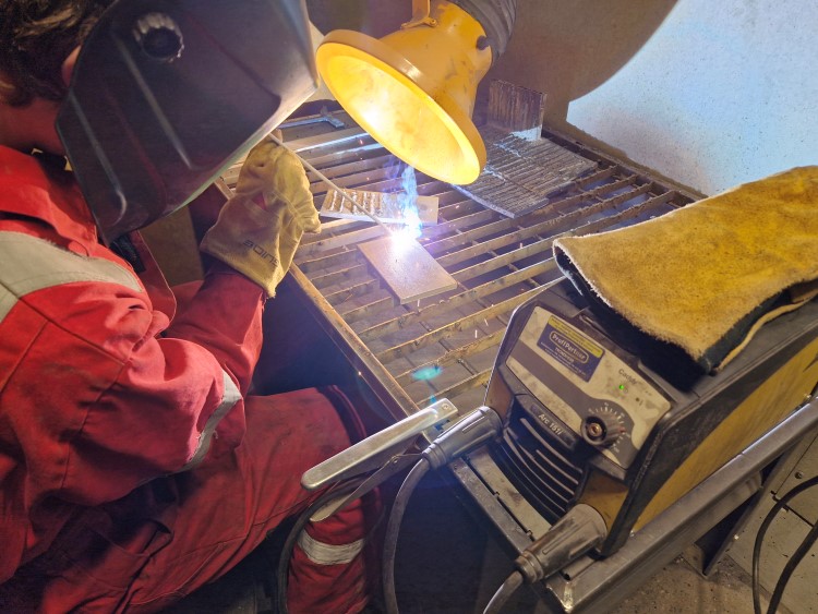 Elev med arbeidshansker og beskyttelsesmaske sveiser